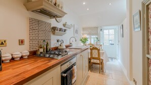 A kitchen with a wooden countertop, a stove, and a sink. There are cabinets and a chair in the background. - New Church Cottage  - sleeps 4 guests  in 2 bedrooms (Tetbury)