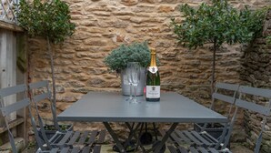 A table with a bottle of champagne, two glasses, and a potted plant. - New Church Cottage  - sleeps 4 guests  in 2 bedrooms (Tetbury)