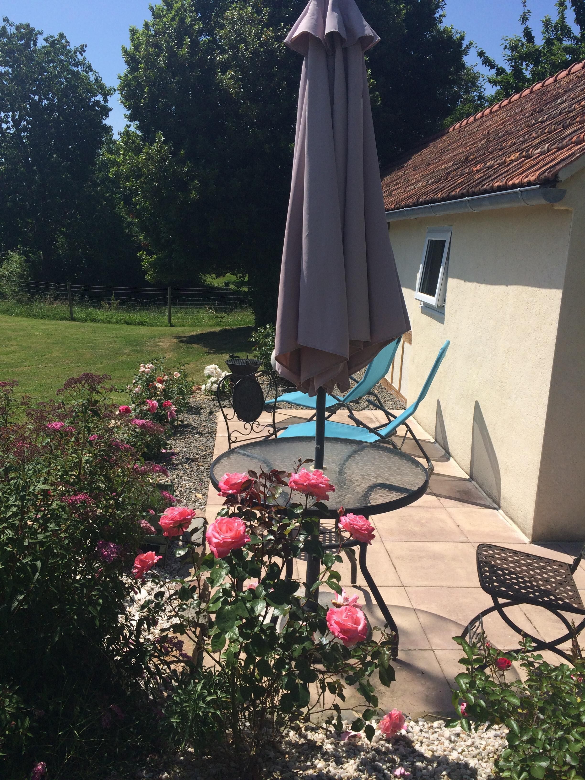 Eine Terrasse mit Tisch und Stühlen, umgeben von blühenden Rosen und einem kleinen Garten.