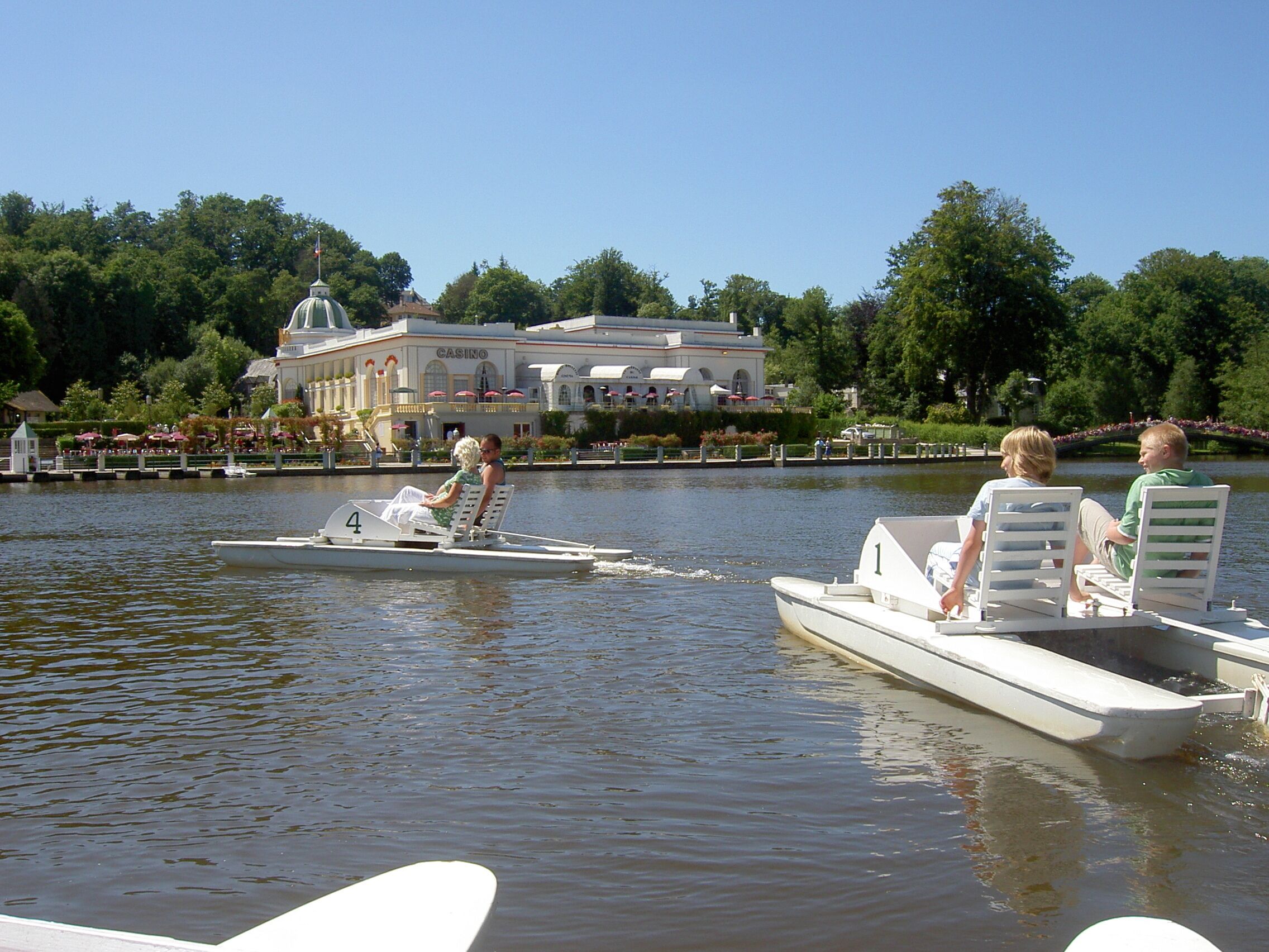 Un bateau avec deux personnes et un enfant à bord, un bâtiment de casino en arrière-plan et un lac paisible.