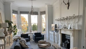 A spacious living room with a fireplace, large windows, and a chandelier. - High View Large Luxury House (London)