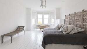 A bedroom with a bed, a bench, a bathtub, and a decorative wall panel. - High View Large Luxury House (London)
