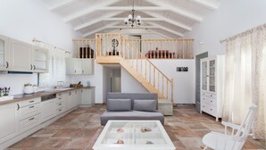 A spacious kitchen with white cabinets, a wooden staircase, a grey sofa, and a rocking chair.