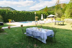 Un coin repas avec une table dressée pour six personnes, entourée de chaises, et une piscine avec des chaises longues en arrière-plan.