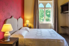 Une chambre d’hôtel avec un lit, deux lampes de chevet, un téléviseur posé sur une étagère et une fenêtre avec des rideaux.