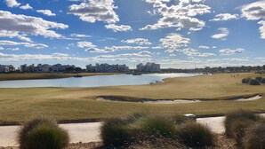 A golf course with a lake, buildings in the background, and a clear sky.