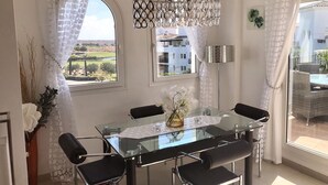 A dining area with a glass table, black chairs, and a view of buildings and greenery outside.