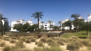 A coastal hotel with white buildings, palm trees, and a sandy landscape.