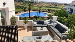A balcony with a pool, outdoor furniture, and a view of a golf course.