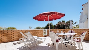 An outdoor patio with a table and chairs, a red umbrella, and a brick wall. - Apartment Tropicos (Carvoeiro)