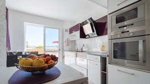 A modern kitchen with white cabinets, stainless steel appliances, and a large window offering a view of the outdoors. - Apartment Tropicos (Carvoeiro)