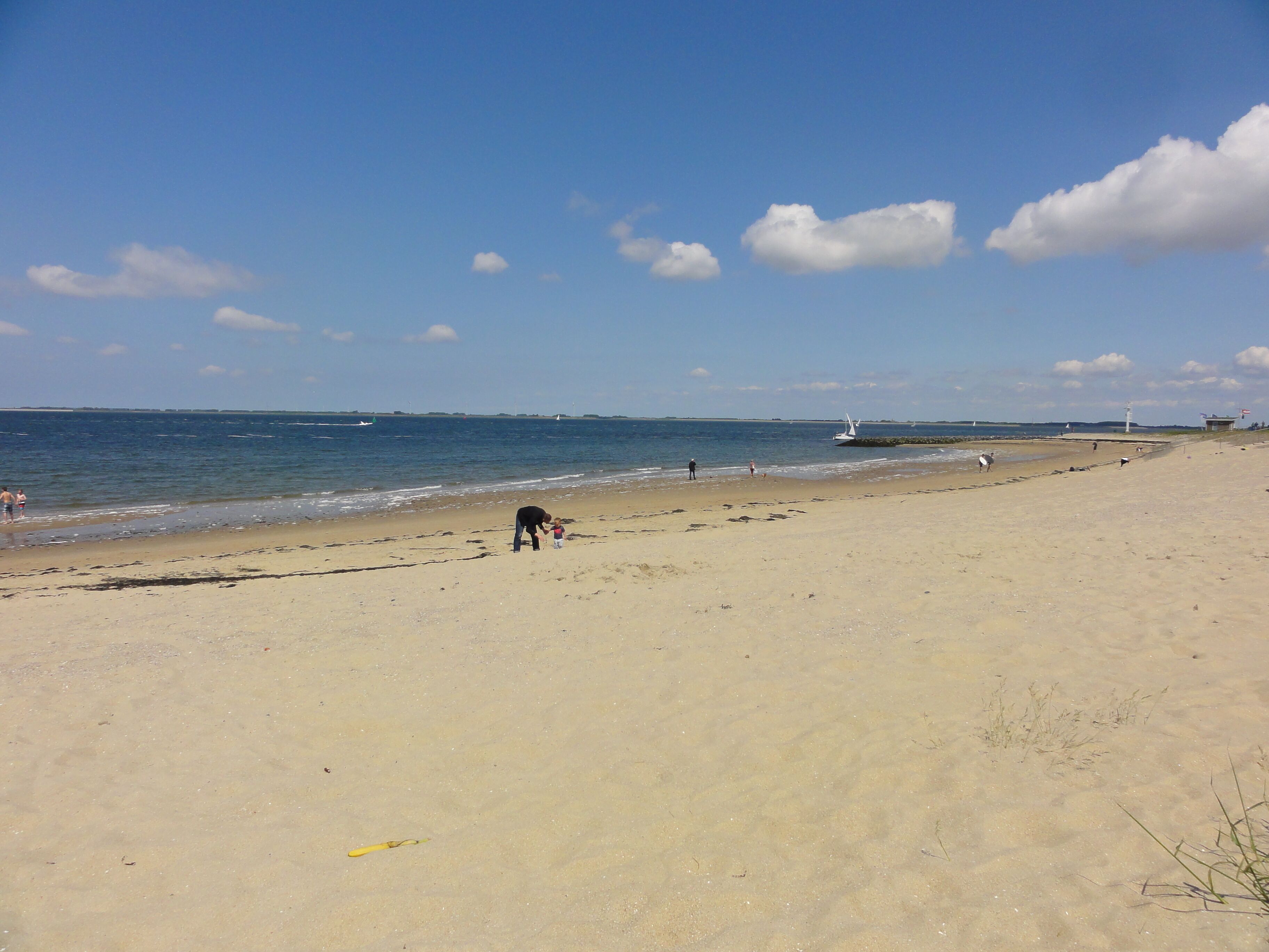 A wide sandy beach with gentle waves, a clear sky, and a few boats in the distance.