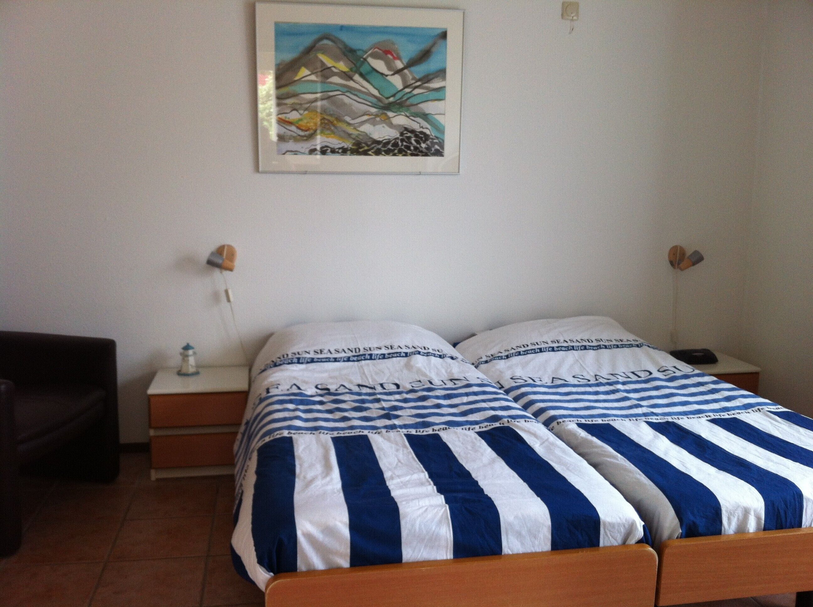 A bedroom with a bed featuring striped bedding, a nightstand with a lamp, and a wall-mounted painting.