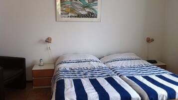 A bedroom with a bed featuring striped bedding, a nightstand with a lamp, and a wall-mounted painting.