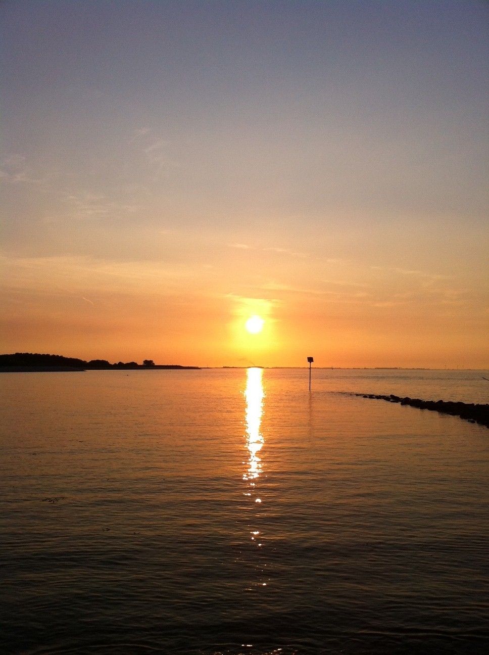 A sunset over a calm body of water with a distant shoreline.