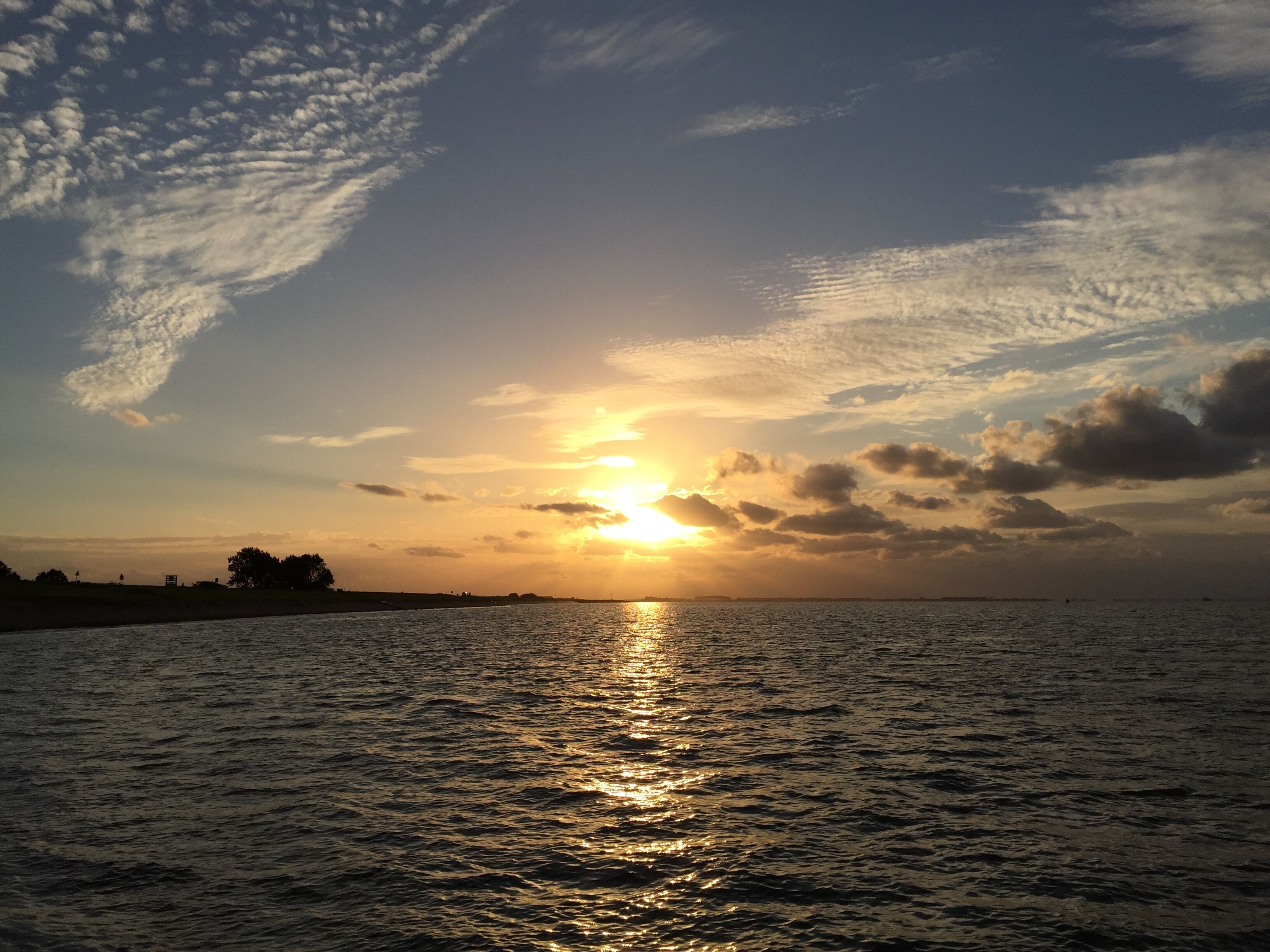 A sunset over a calm body of water with a distant shoreline.