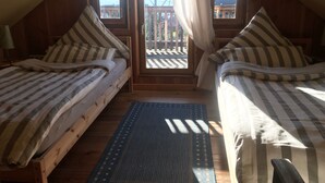 Un dormitorio cálido en el ático con dos camas individuales, vista al balcón y piso de madera.