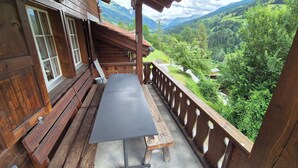 Un balcon en bois, agrémenté d’une table et de bancs, qui offre une vue sur un paysage montagneux.