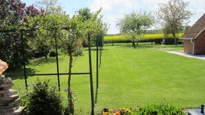 Ein gepflegter Garten mit Rasenfläche, verschiedenen blühenden Pflanzen und einem Backsteinhaus.