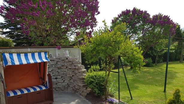 Ein Garten mit Steinmauer, einer Holzbank mit Streifenveranda und einem Blumenbehang Rasen.