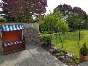 Ein Garten mit Steinmauer, einer Holzbank mit Streifenveranda und einem Blumenbehang Rasen.