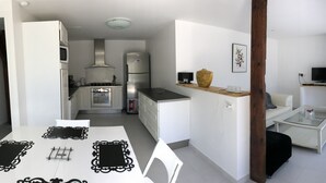 A modern kitchen with white cabinets, a microwave, and a refrigerator. There is a dining table with black table runners and white chairs. A small sofa and a glass coffee table are in the living area. - Independent house with heated pool (Perigord Noir hamlet) (CARLUX)