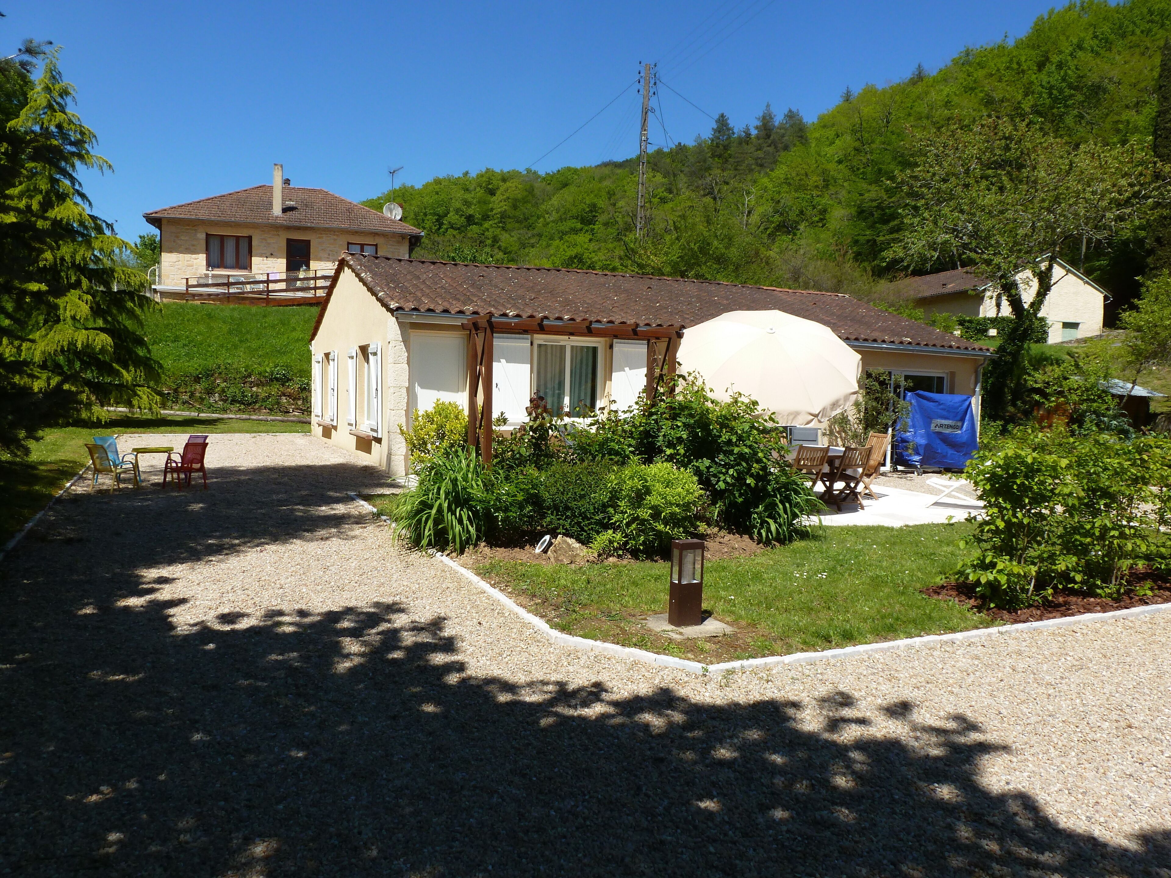 A house with a gravel driveway, a covered patio, and a garden with shrubs and a lantern.