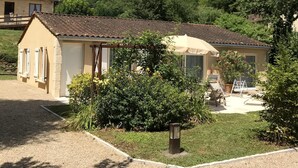 A two-story house with a tiled roof, a garden with various plants, and a patio area with outdoor furniture. - Independent house with heated pool (Perigord Noir hamlet) (CARLUX)