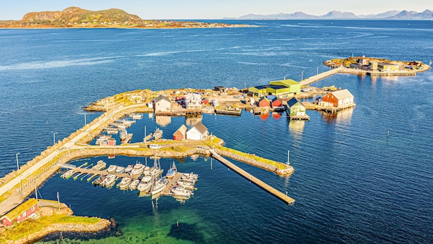 An aerial view of a coastal town with a marina, houses, and a mountainous backdrop.