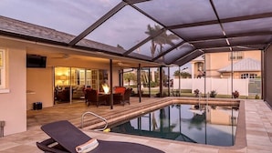 Ein Schwimmbad mit Liegestühlen, einer überdachten Terrasse und einer Feuerstelle.