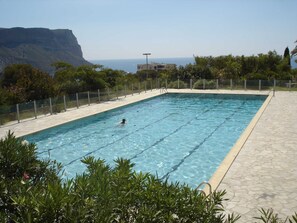 A rectangular swimming pool with clear blue water, surrounded by a stone deck and a metal fence. In the background, there is a cliff and a building. - Sea views from a beautiful building, ideally located in Cassis near the harbour (Cassis)