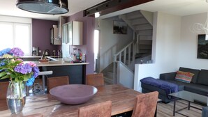 A modern kitchen with a dining area, a staircase, and a living room with a sofa and a coffee table. - Bright tastefully decorated house 300 meters from the Sables Blancs beach. (Concarneau)