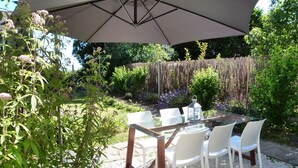 An outdoor patio with a glass table and white chairs, surrounded by gravel and greenery. - Bright tastefully decorated house 300 meters from the Sables Blancs beach. (Concarneau)