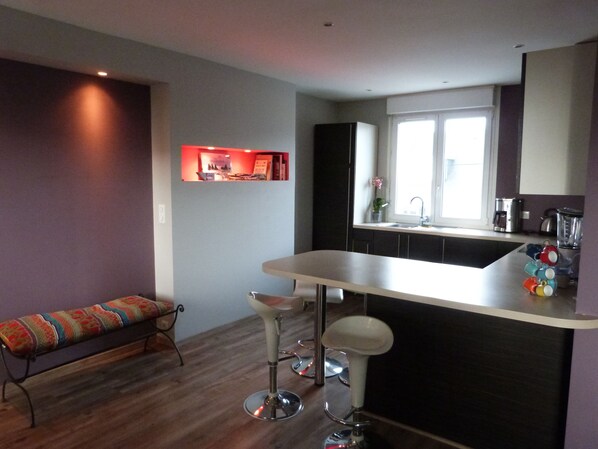 A modern kitchen with a bar area, a bench, and a window with natural light. - Bright tastefully decorated house 300 meters from the Sables Blancs beach. (Concarneau)
