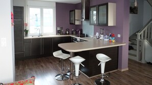 A modern kitchen with dark cabinets, a large island with bar stools, and a window providing natural light. - Bright tastefully decorated house 300 meters from the Sables Blancs beach. (Concarneau)