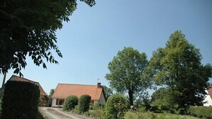 Una casa rural con techo de tejas rojas, rodeada de vegetación y un camino de tierra.