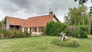 Una casa rústica con techo inclinado y chimenea, rodeada de un patio cubierto de césped y abundante follaje.