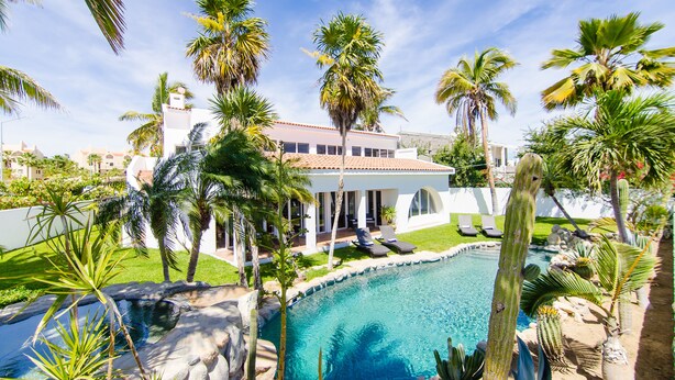 A pool surrounded by palm trees and a white building with a red roof. - Amazing 6,000 sqft house sleeps 10, walk to Beach, Shops and Restaurants (San José del Cabo)