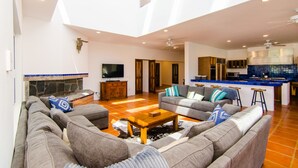A spacious living room with a large sofa set, a coffee table, and a television. There is a kitchen area with a blue backsplash and a bar counter. - Amazing 6,000 sqft house sleeps 10, walk to Beach, Shops and Restaurants (San José del Cabo)