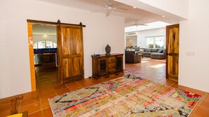A spacious living area with a large, colorful rug, wooden furniture, and a sliding door leading to a kitchen. - Amazing 6,000 sqft house sleeps 10, walk to Beach, Shops and Restaurants (San José del Cabo)