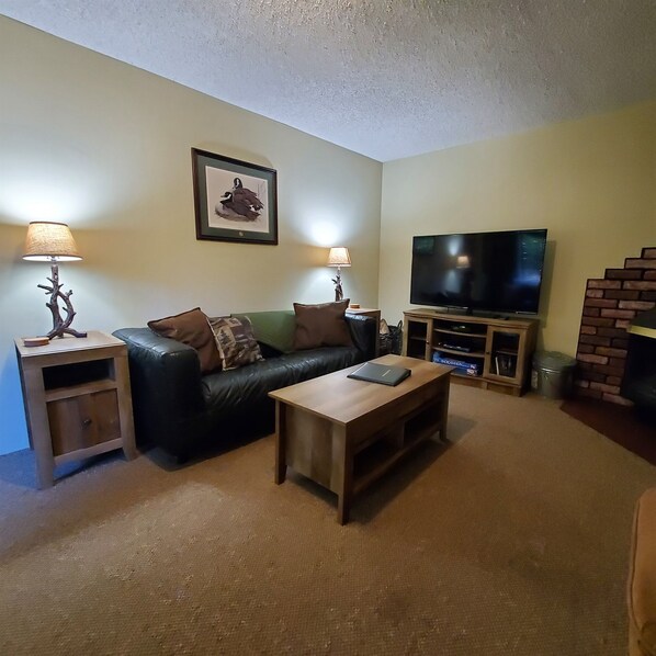 A living room with a leather sofa, two side tables with lamps, a wooden coffee table, a flat-screen TV, and a framed picture on the wall. - River Run, Near Mossbra Falls & River access. (Dunsmuir)