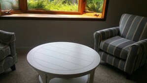 A round white table with a simple design, positioned between two patterned armchairs in a room with a view of greenery through a window. - Golf - Winery - Hike - Bike (Grand Junction)