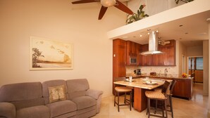 Une cuisine moderne avec des meubles en bois, un coin repas doté d’une table en marbre et un ventilateur de plafond.