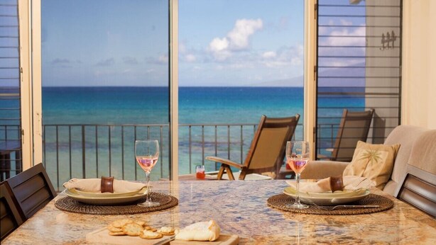 Un coin repas avec vue sur l’océan, deux chaises, une table avec des assiettes et des verres, et un canapé.