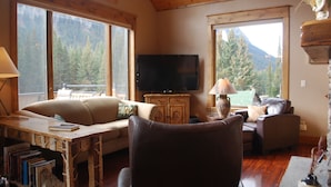 Una sala de estar acogedora con techo de madera, un televisor de pantalla plana, un sofá, una mesa de centro y una estantería.