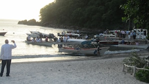 Een strand met diverse boten die aanmeren en mensen daarop.