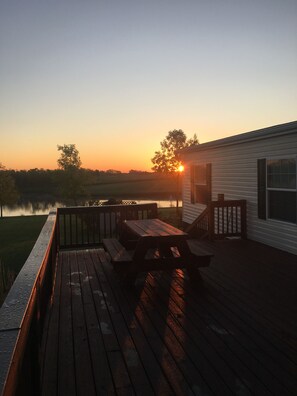 A wooden deck with picnic tables and a view of a lake at sunset. - Looking for a getaway? This property is perfect for your vacation! (Weldon)