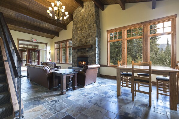 A spacious living area with a stone fireplace, wooden furniture, and large windows offering a view of the outdoors.