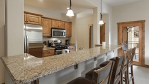 A kitchen with granite countertops, stainless steel appliances, wooden cabinets, and bar stools.