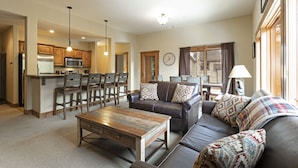 A spacious living room with a sofa, coffee table, and dining area with chairs and a kitchen in the background.